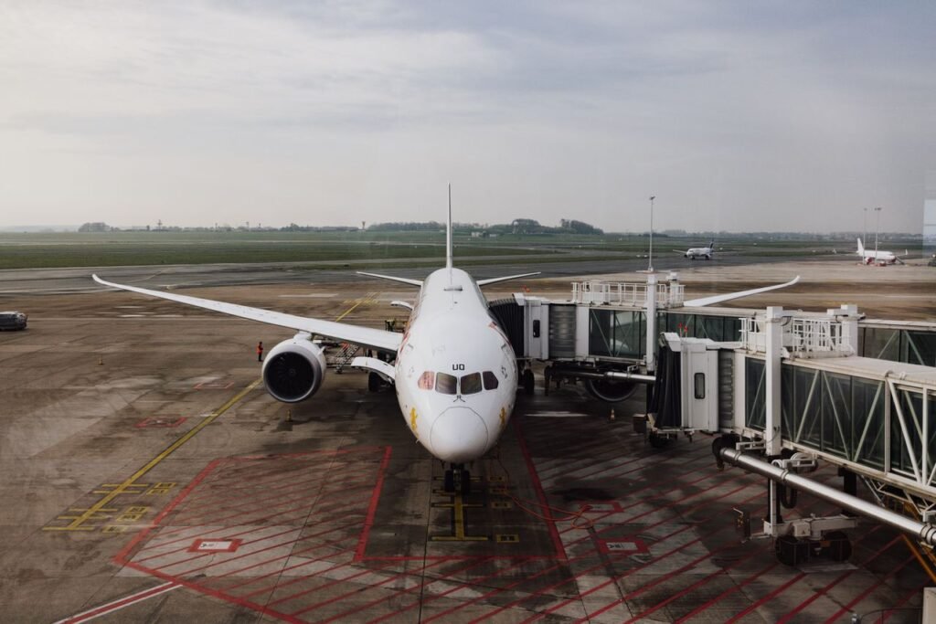 pexels-photo-16562841-16562841 A modern jet airplane docked at an airport terminal gate, ready for boarding on a cloudy day.