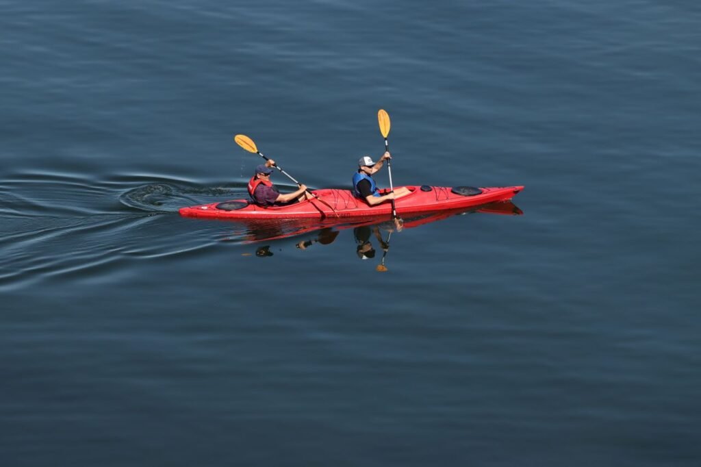 Two people kayaking in a red kayak on a serene lake in Sweden. Outdoor recreation and adventure.