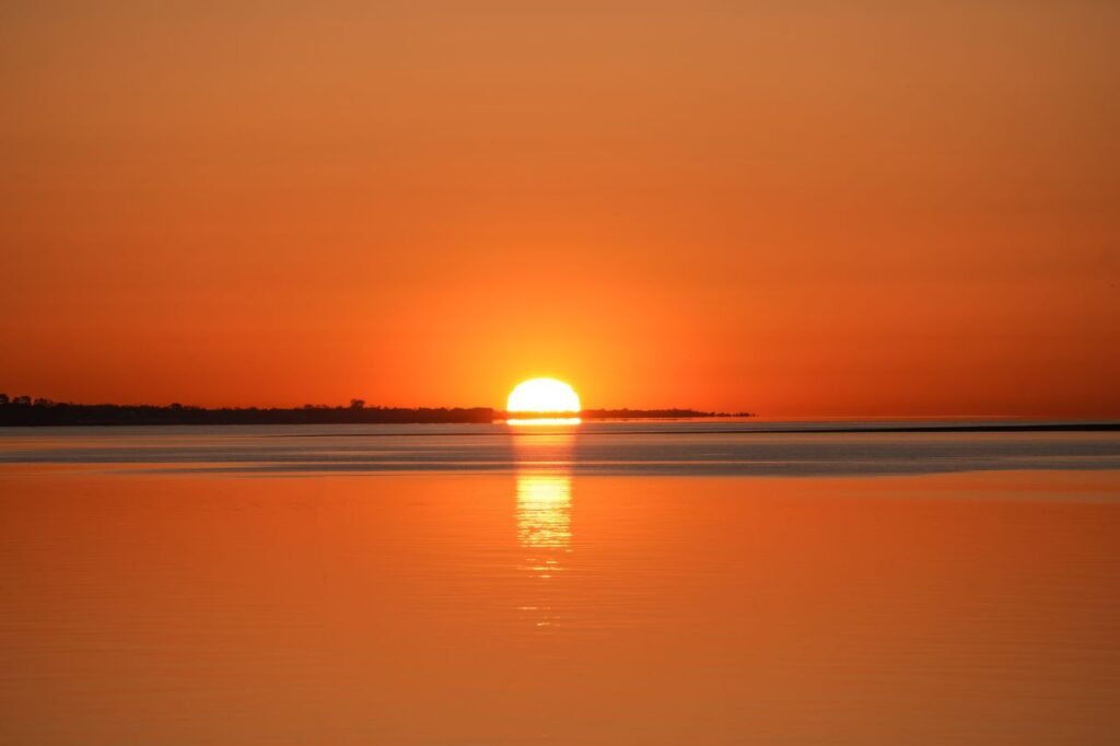 A tranquil sunset scene with vibrant orange hues reflecting on the calm ocean waters.